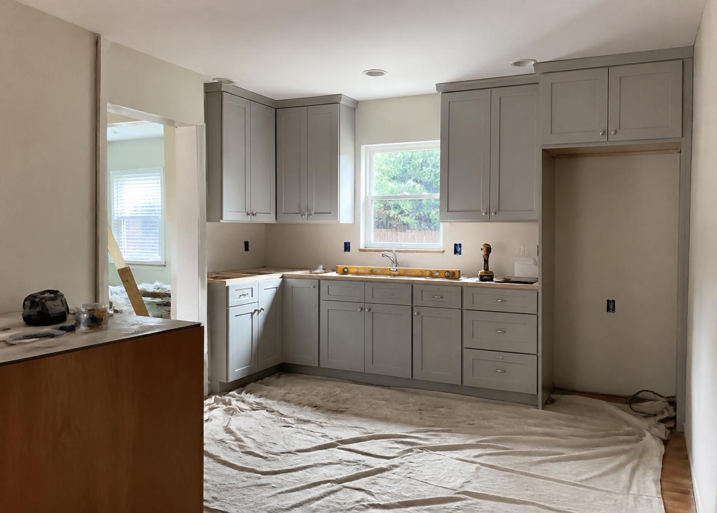 Kitchen mid-renovation with newly installed cabinets, drop cloths on the floor, and tools on the counter
