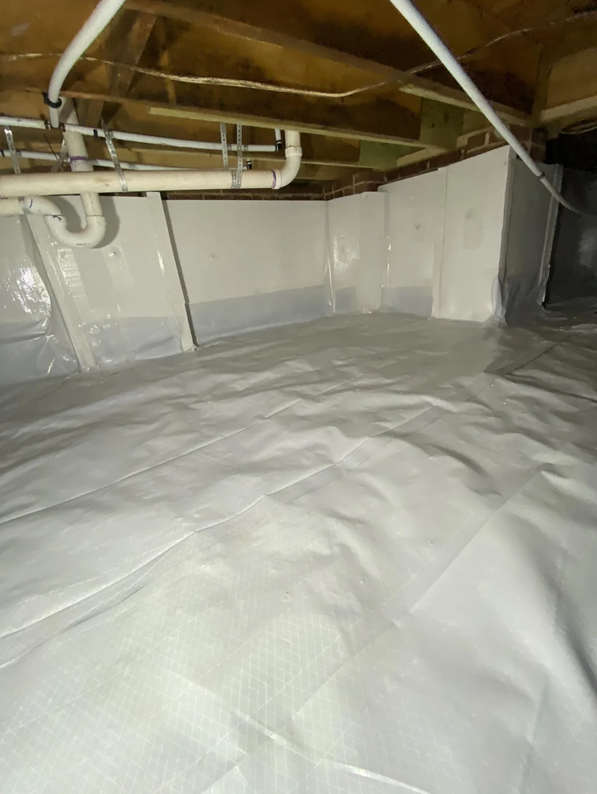 Same crawlspace fully encapsulated with a sealed white vapor barrier across the ground and walls