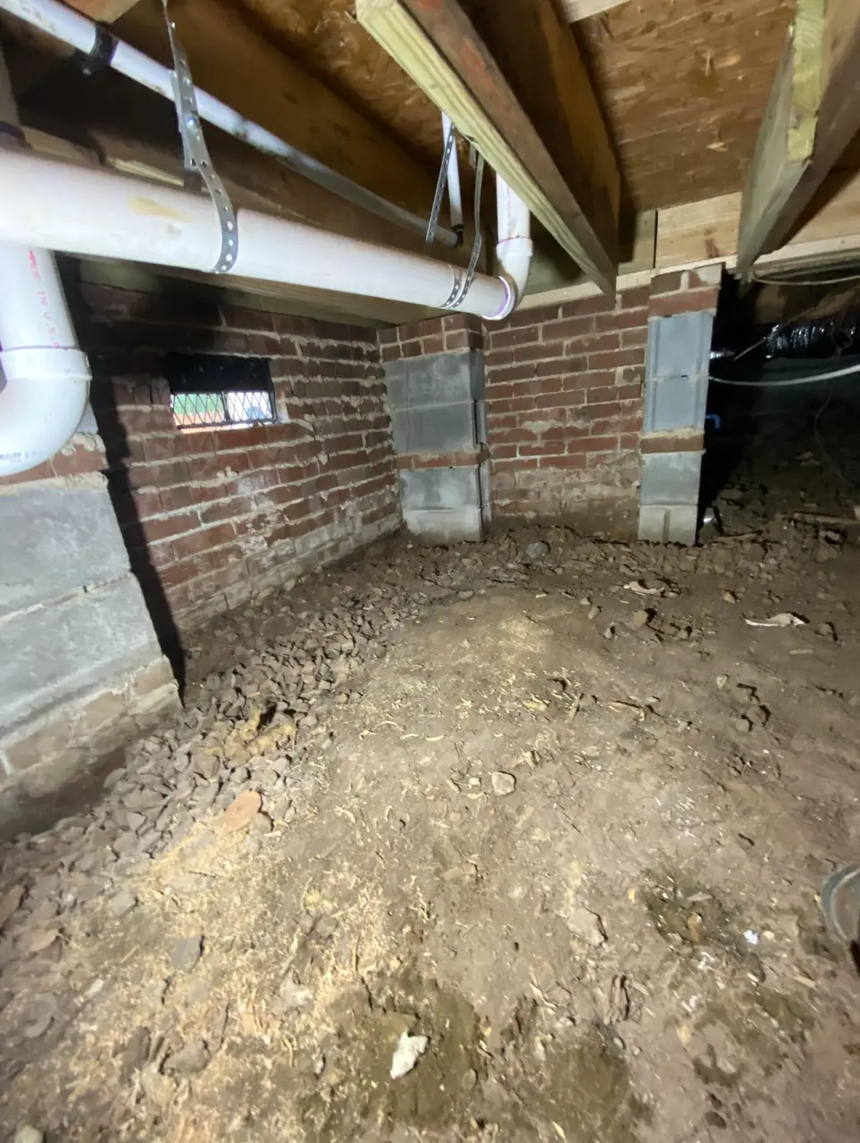 Unfinished crawlspace with bare dirt floor and exposed brick foundation wall