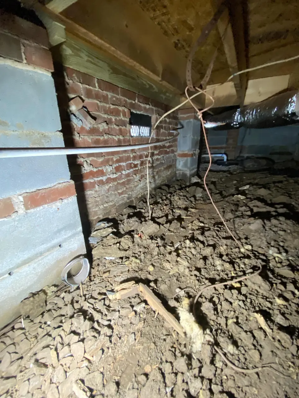 Crawlspace corner with brick foundation wall and exposed floor joists before encapsulation