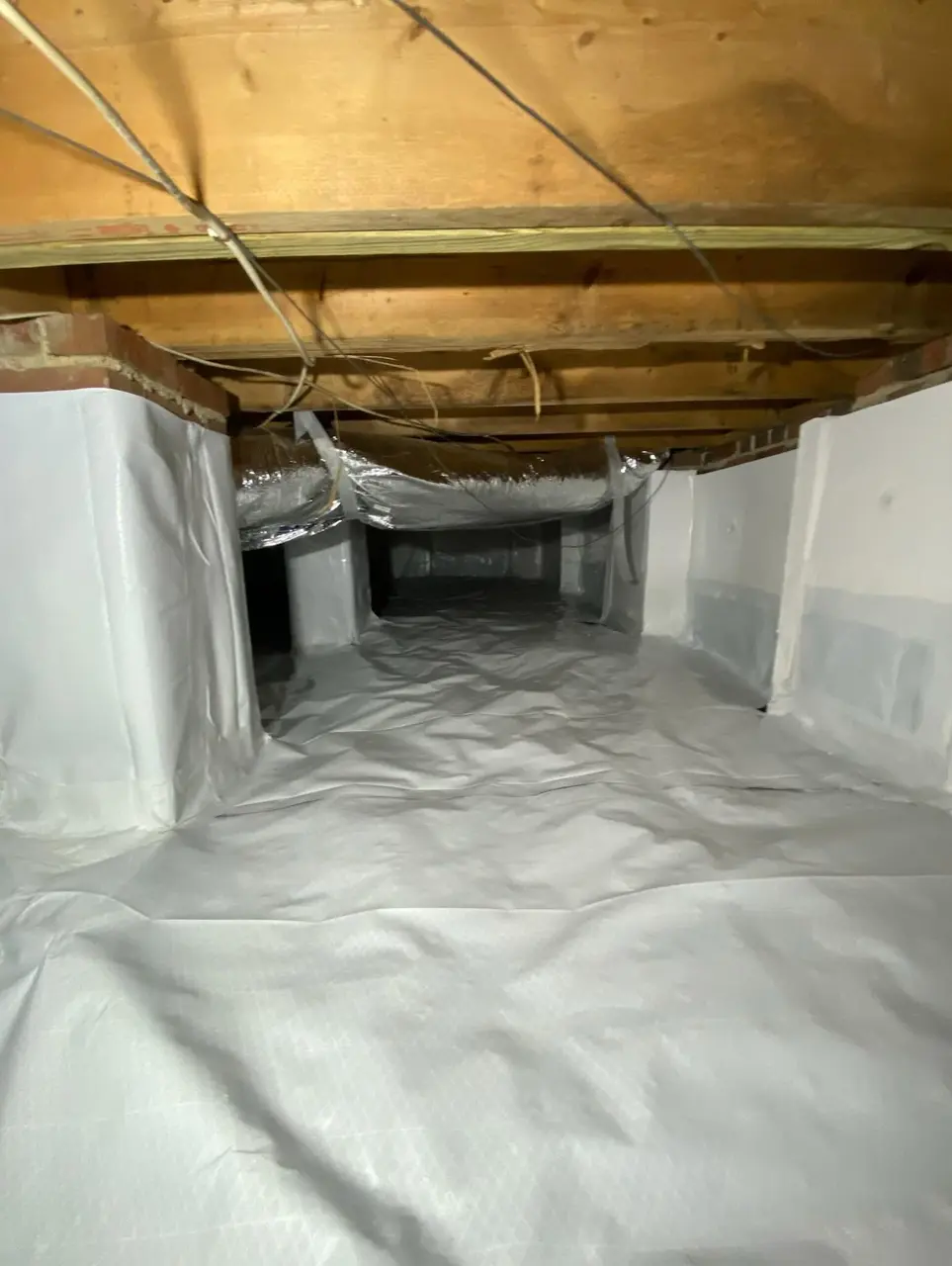 Fully encapsulated crawlspace with white vapor barrier across the ground and walls