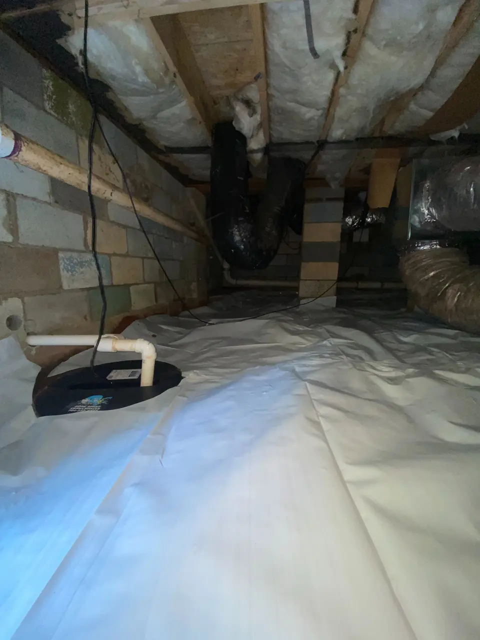 Encapsulated crawlspace with dehumidifier drain line running across the vapor barrier